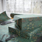 Green patterned gift box with wrapping paper and scissors on a table