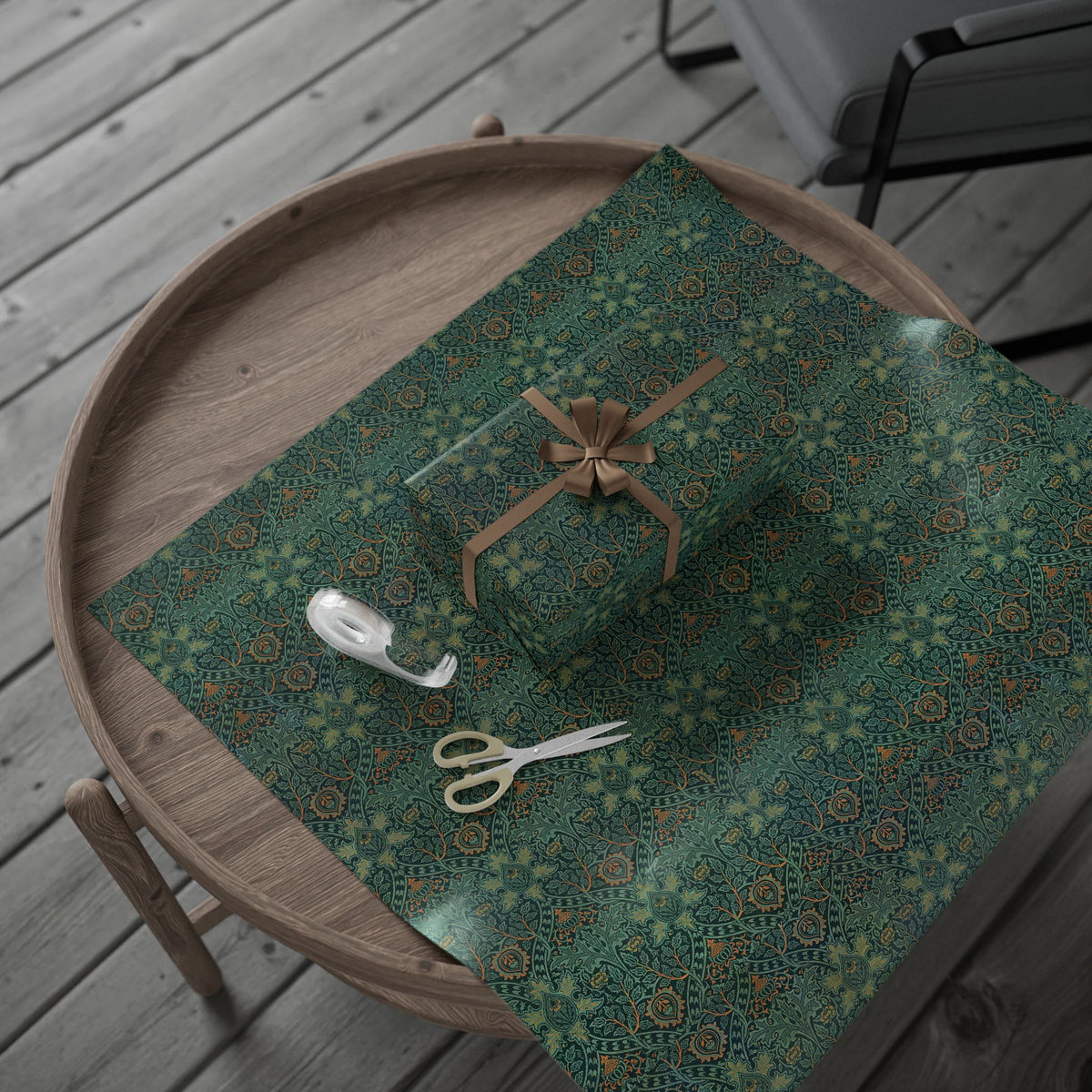 Green patterned fabric with a roll of tape, scissors, and a decorative bow on a wooden surface.