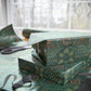 Gift box wrapped in green patterned paper with scissors on a matching tablecloth.