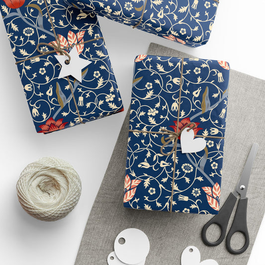 Decorative blue gift wrap with floral and bird pattern, scissors, twine, and tags on a white surface.
