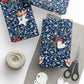 Decorative blue gift wrap with floral and bird pattern, scissors, twine, and tags on a white surface.
