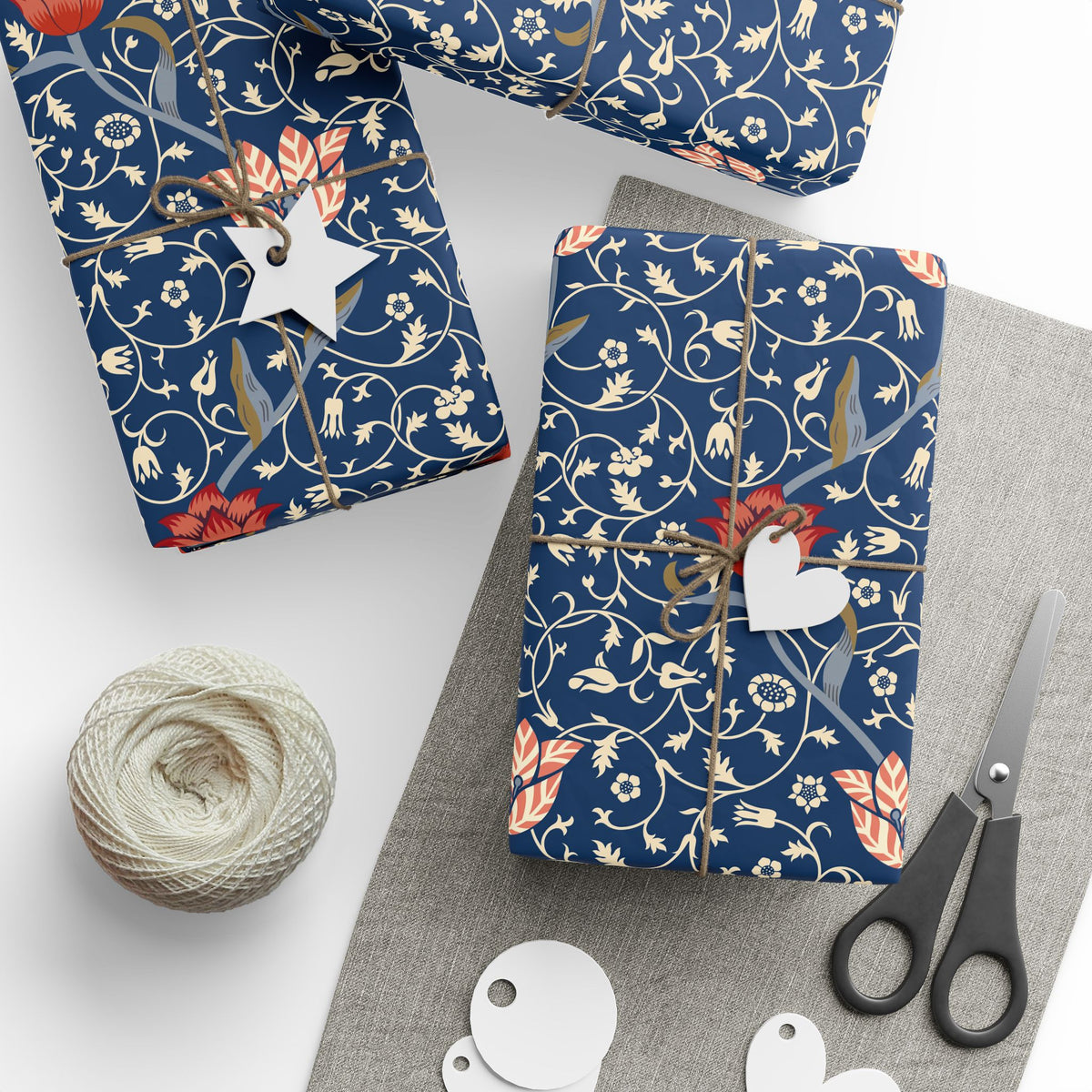 Gift wrap with floral pattern, scissors, twine, and tags on a white surface