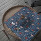 Decorative blue floral placemat on a wooden table with a spider and scissors.