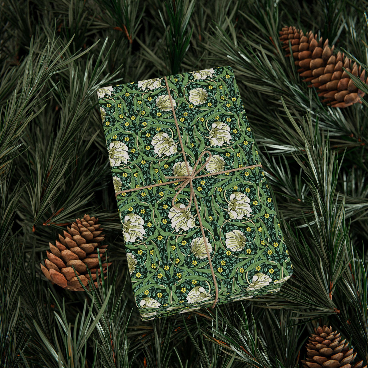 Gift box with floral pattern wrapped in greenery and pine cones