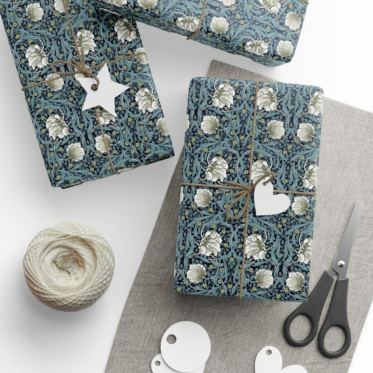 Gift wrap with floral pattern, scissors, and yarn on a white surface