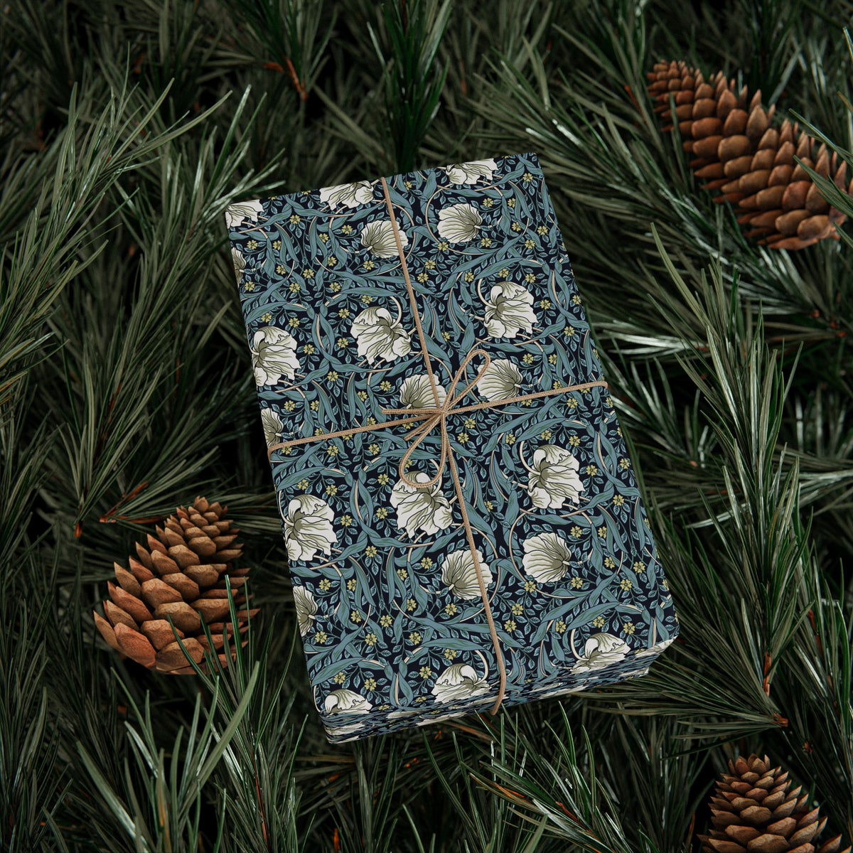 Gift box with floral pattern wrapped in twine on pine branches