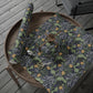 Round wooden table with a floral-patterned cloth, scissors, and a roll of green paper on a wooden deck.