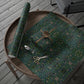 Wooden tray with floral-patterned fabric, scissors, and a roll of green paper on a wooden surface.