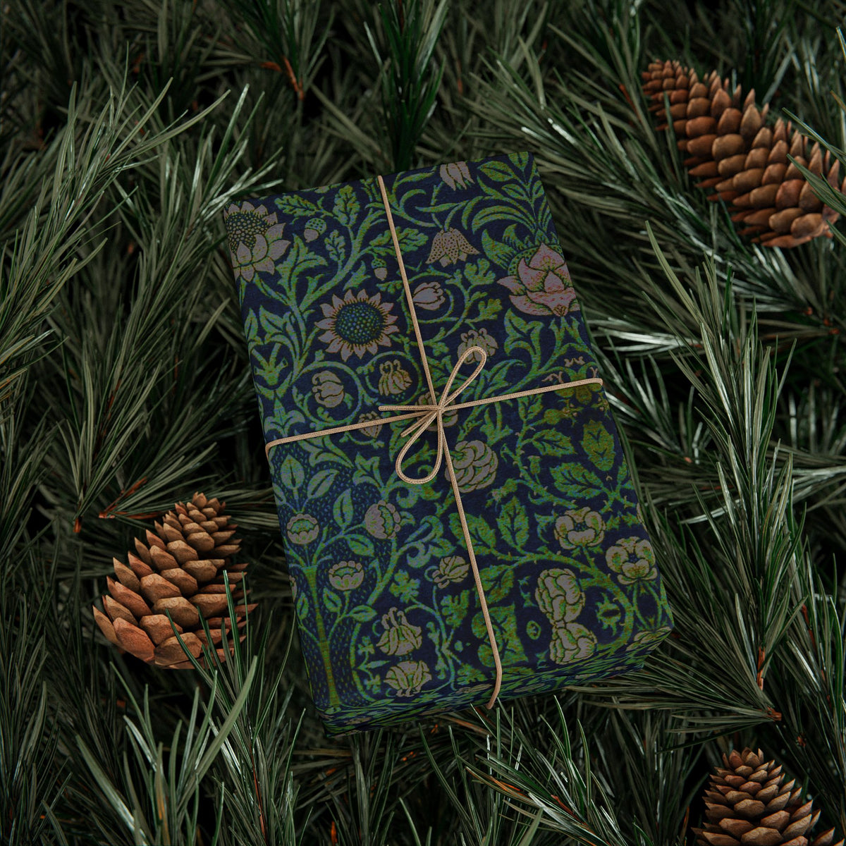 Gift box with green floral pattern and beige ribbon on pine branches with pine cones.