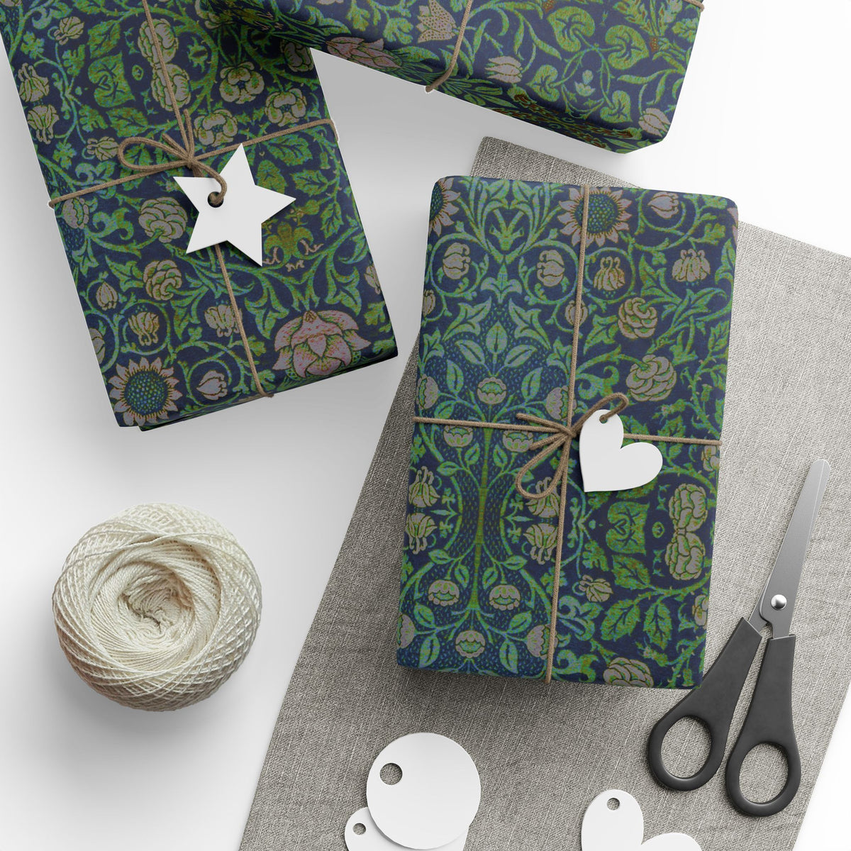 Gifts wrapped in green and blue patterned paper with decorative tags and scissors on a white surface.