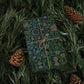 Gift box with green floral pattern and beige ribbon on pine branches with pine cones.