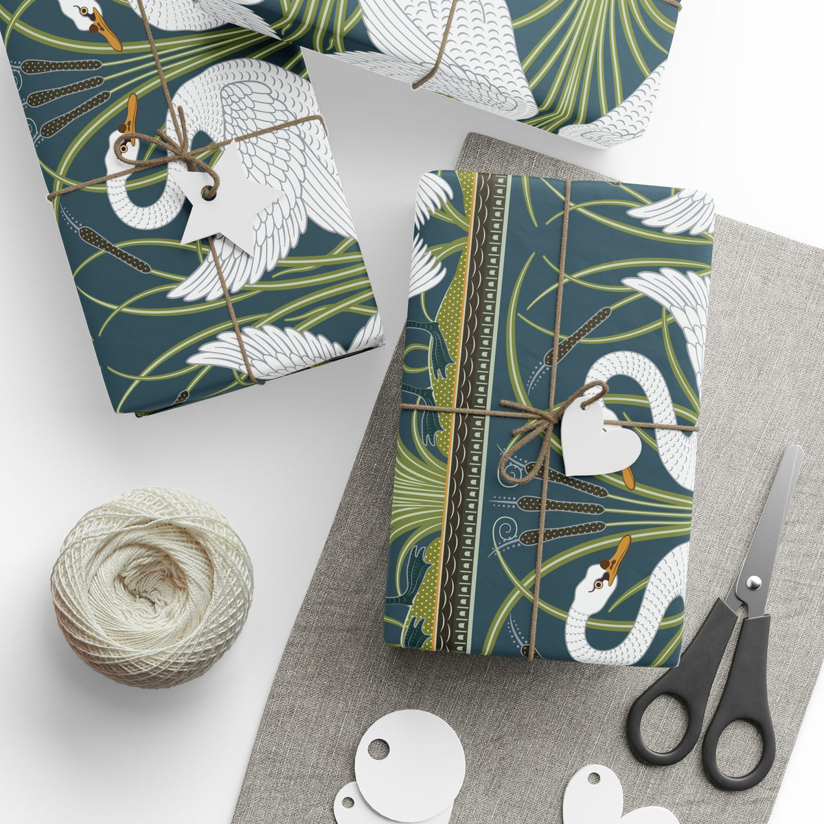 Gift-wrapped items with swan design, scissors, and yarn on a white surface