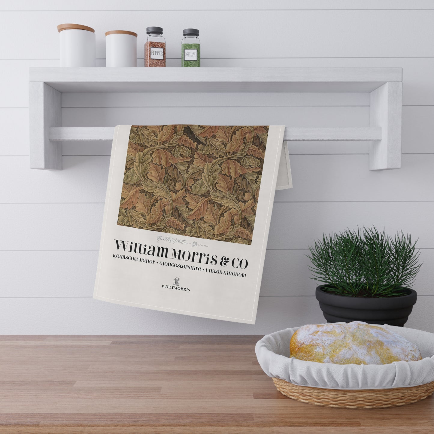 Decorative towel with leaf pattern and 'William Morris & Co' text hanging on a white wall above a wooden shelf.
