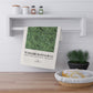 Green patterned towel hanging on a wooden shelf with a plant and basket in the foreground.