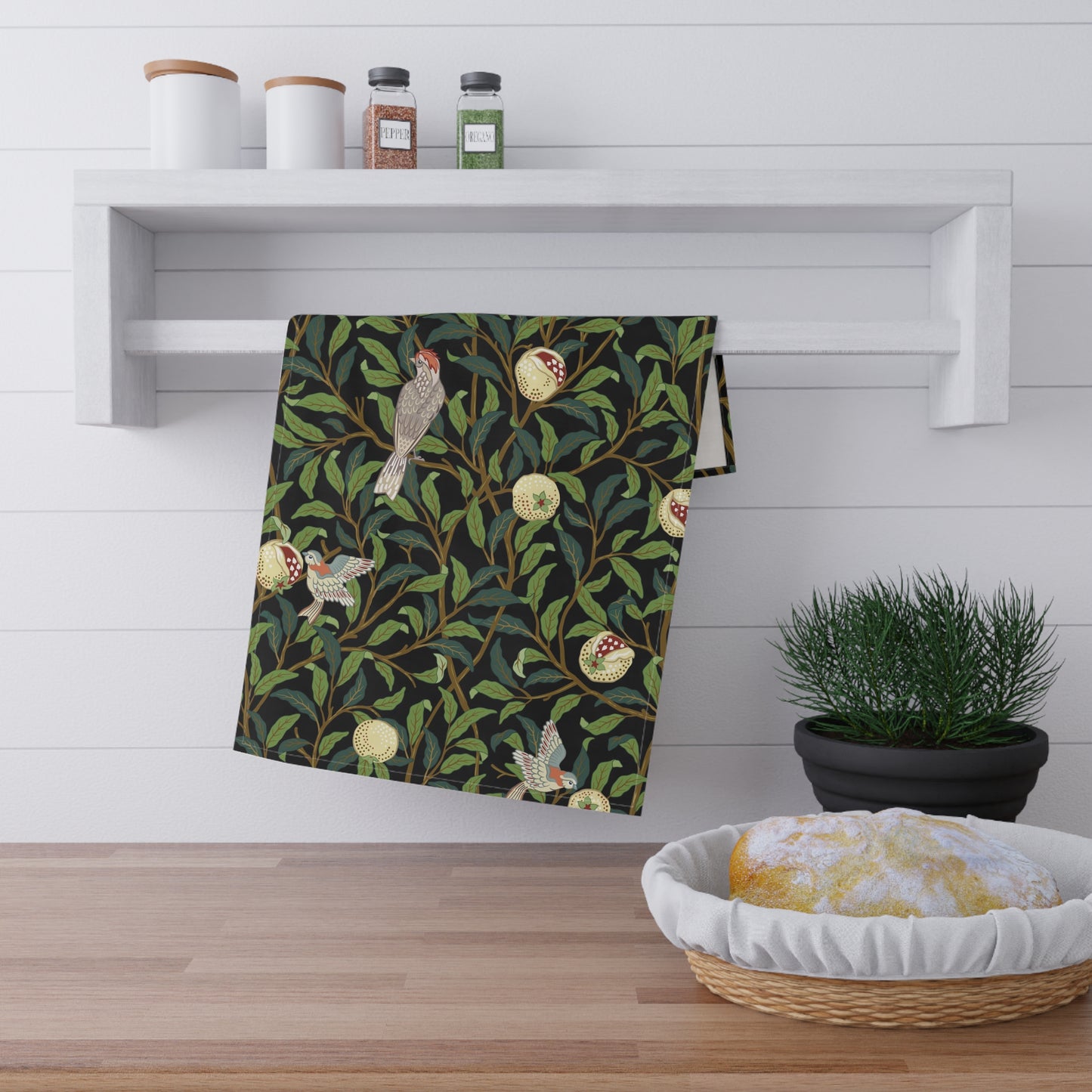 A kitchen tea towel with a design inspired by William Morris, featuring birds and pomegranate patterns on a dark background.