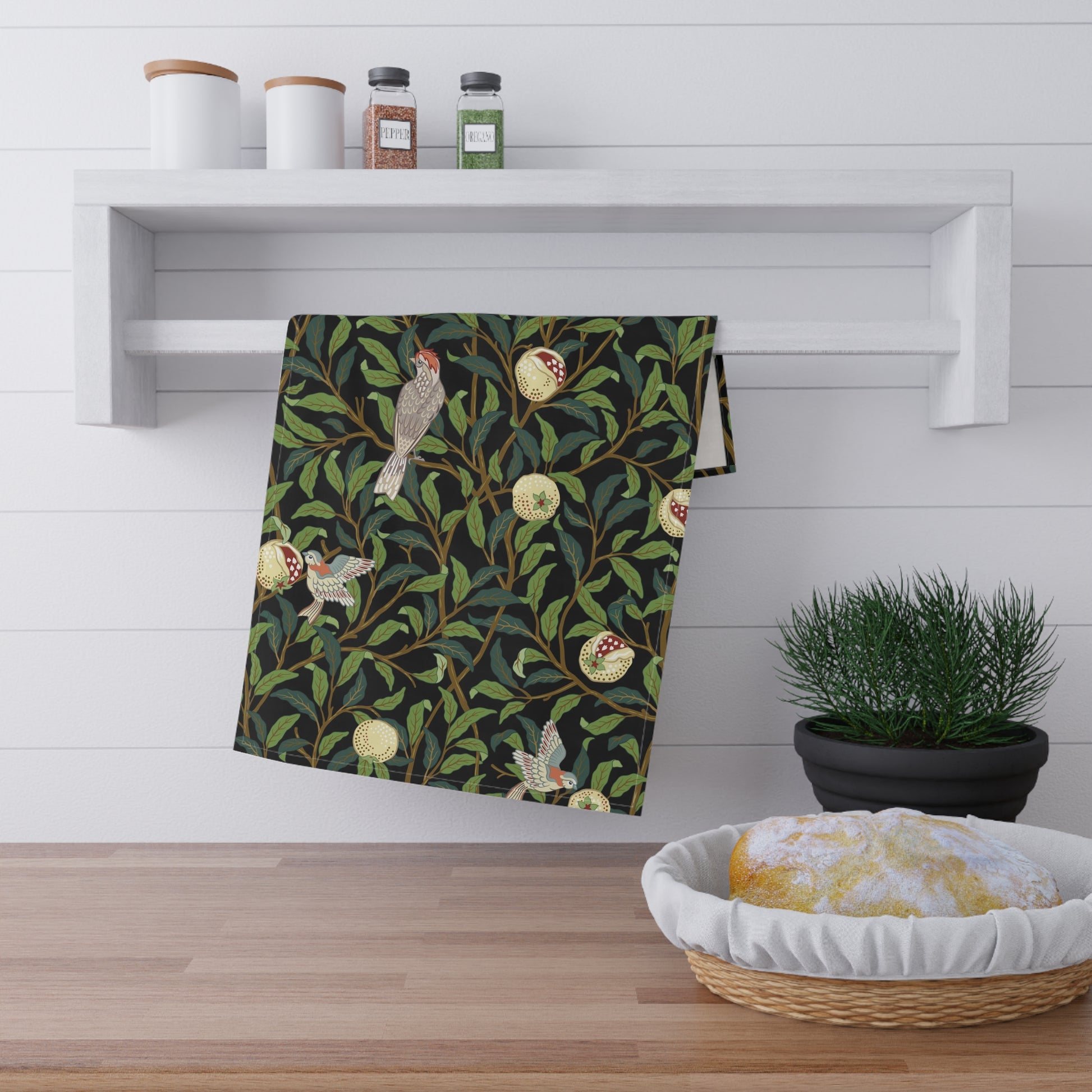 A kitchen tea towel with a design inspired by William Morris, featuring birds and pomegranate patterns on a dark background.