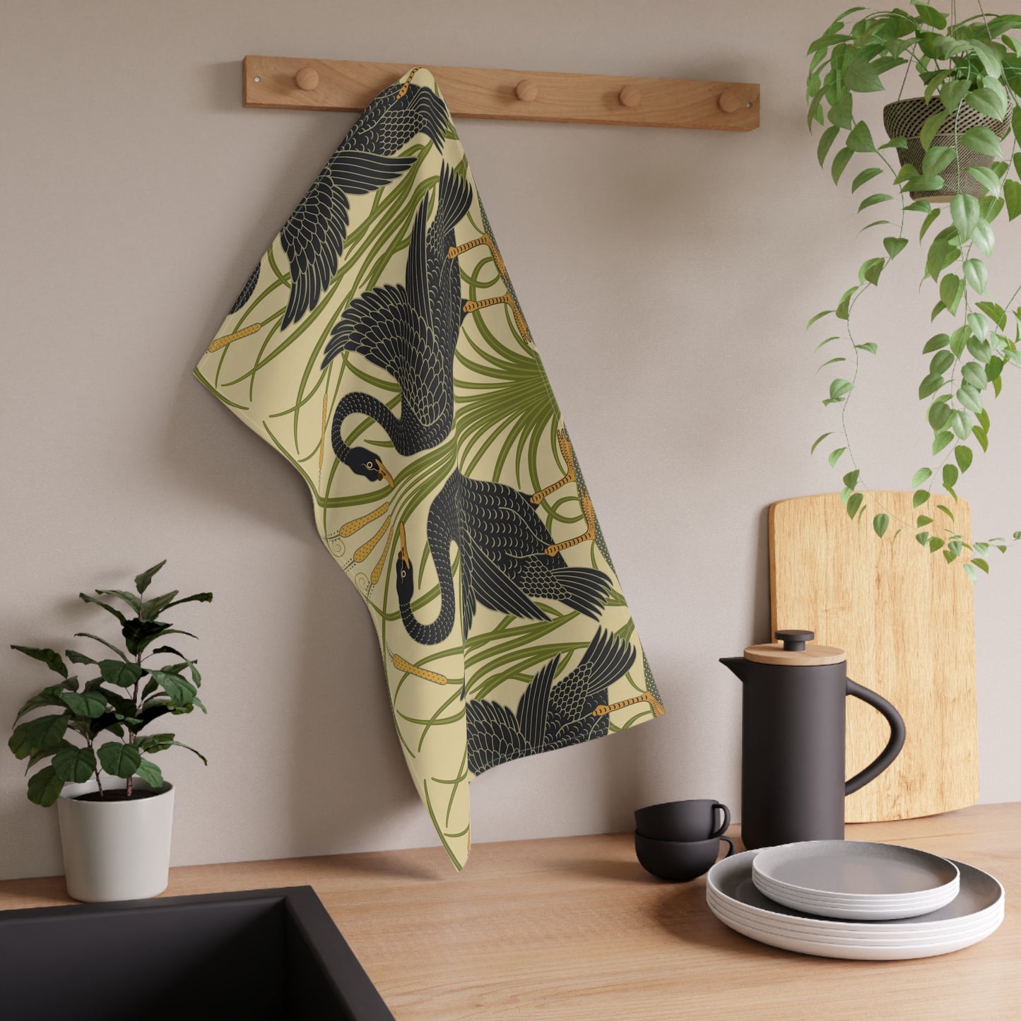 A kitchen tea towel with a repeating William Morris & Co pattern of black swans and green foliage on a beige background.