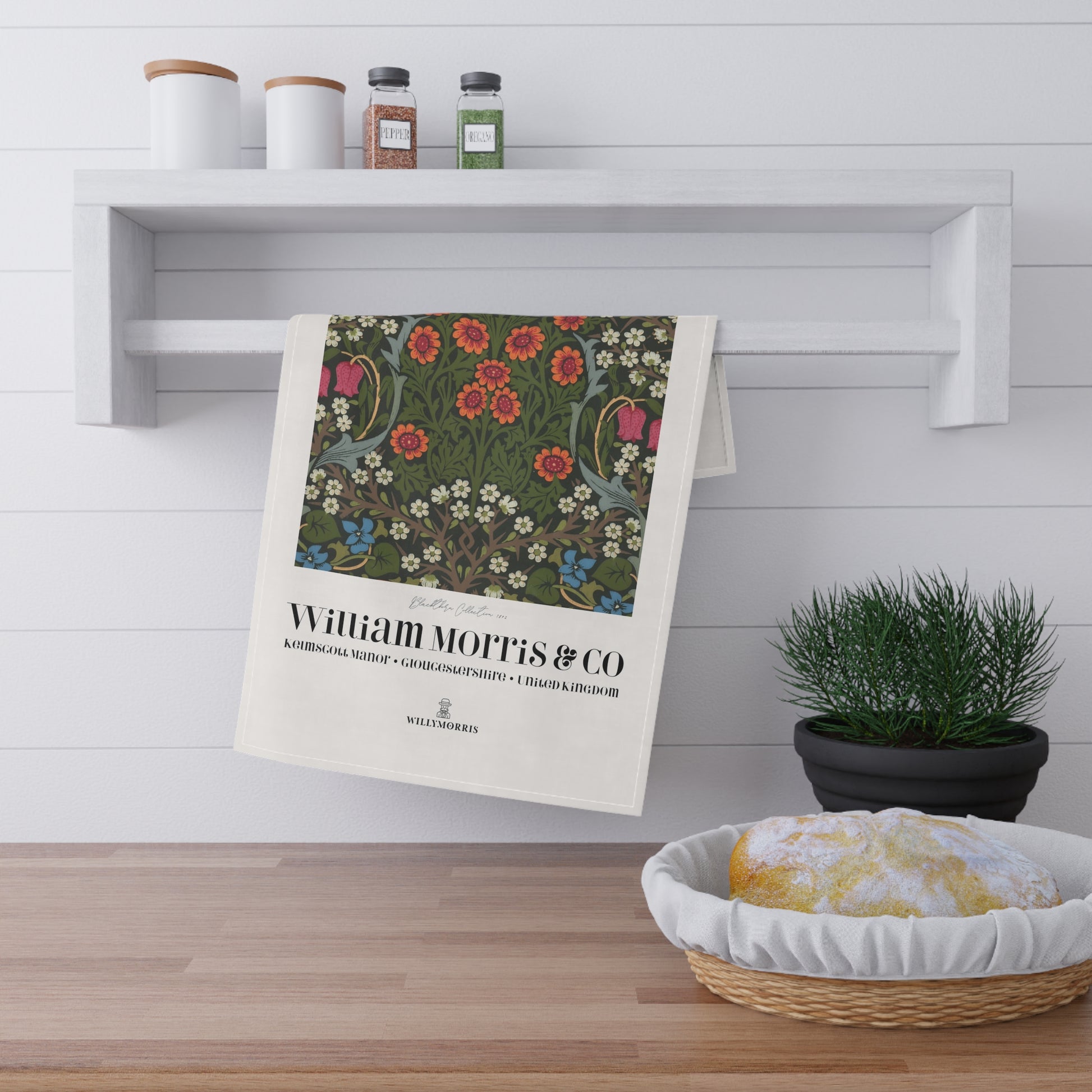 Floral towel hanging on a wooden shelf with a plant and bread basket in the foreground.
