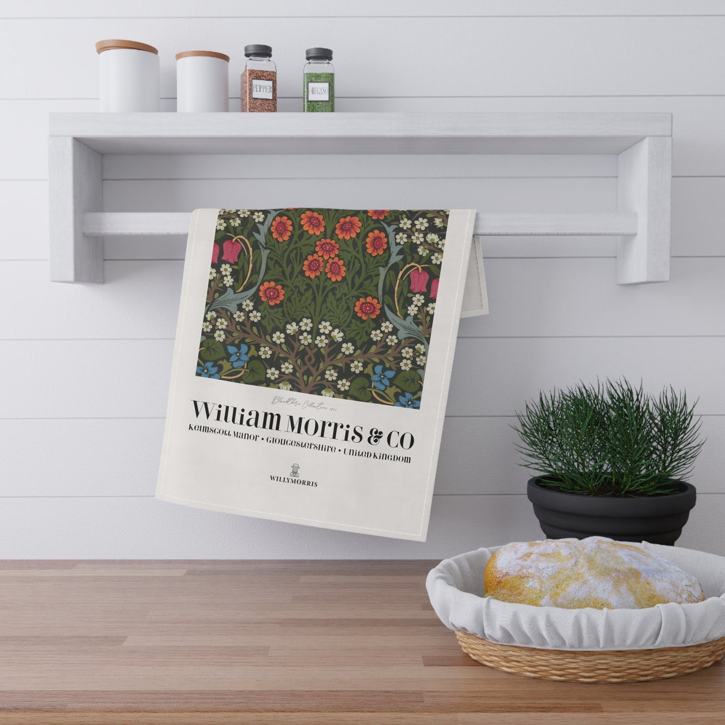 Floral towel hanging on a wooden shelf with a plant and bread basket in the foreground.