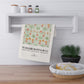 Floral patterned towel hanging on a wooden shelf with a plant and basket in the foreground.