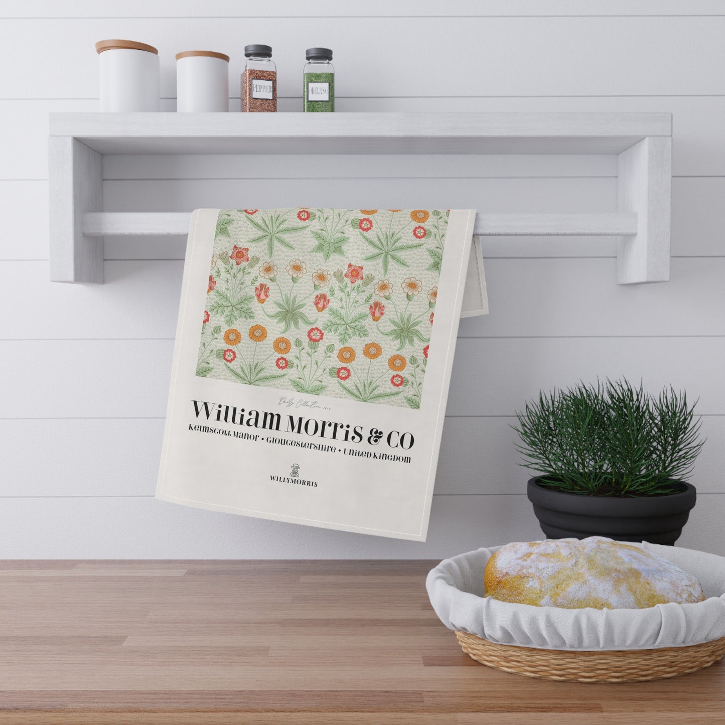 Floral towel hanging on a shelf with a basket of bread and potted plant in the foreground.