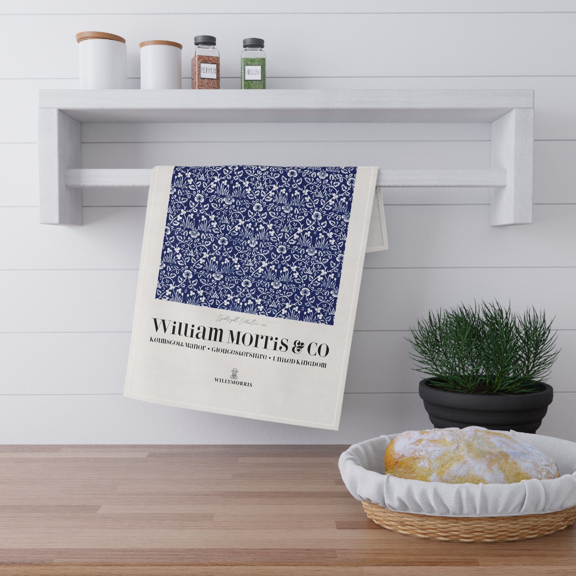 Tea towel with blue floral pattern and 'William Morris & Co' text hanging on a white shelf.