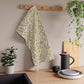 Floral towel hanging on a wooden rack with kitchen items and plants in the background