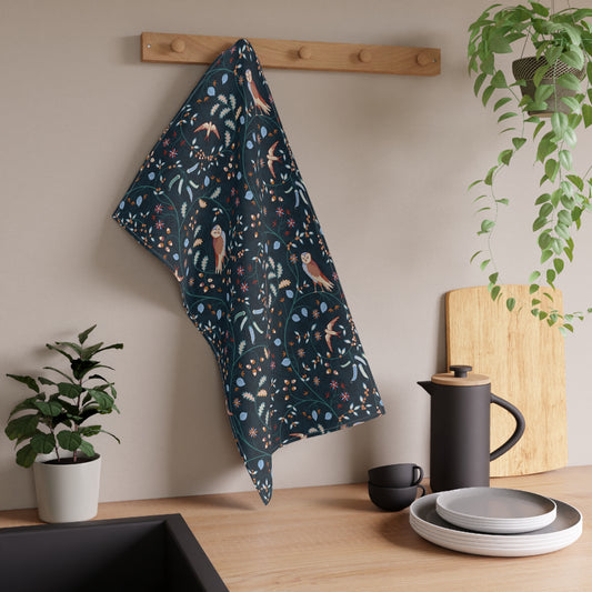 Decorative William Morris & Co tea towel with owl pattern hanging on a white shelf above a wooden surface with a basket and bread.