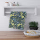 A rectangular kitchen tea towel featuring a floral Arts & Crafts pattern from William Morris & Co with blue flowers and green leaves on a cream background.
