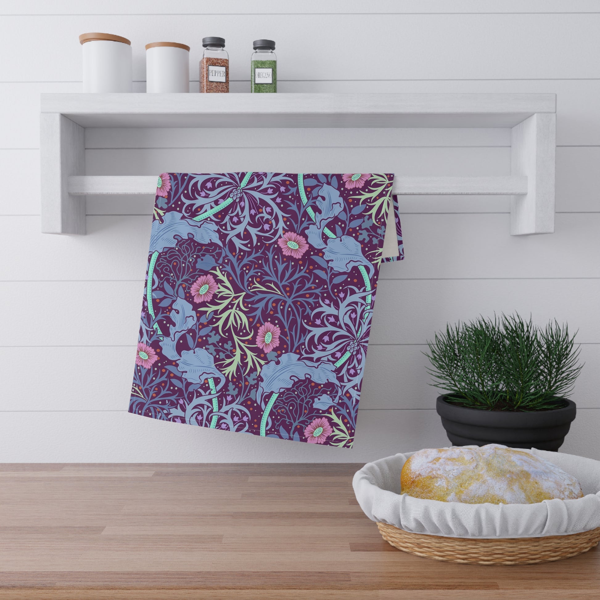 A kitchen tea towel featuring a repeating pattern of seaweed and pink flowers on a purple background.