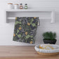 A rectangular kitchen tea towel featuring a repeating pattern of seaweed and yellow flowers on a green background.