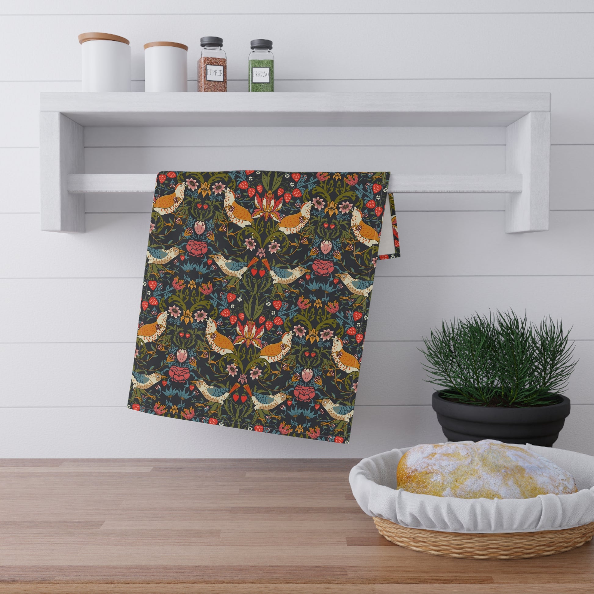 A kitchen tea towel with a repeating pattern featuring birds, flowers, and leaves in dark background, inspired by William Morris' Strawberry Thief design.