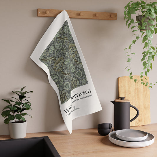 Tea towel with green pattern and text hanging on a wooden rack in a kitchen setting.