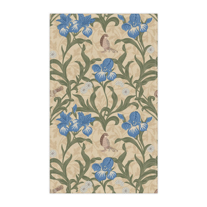 A kitchen tea towel with a William Morris & Co floral pattern featuring blue irises, birds, and a beige background.