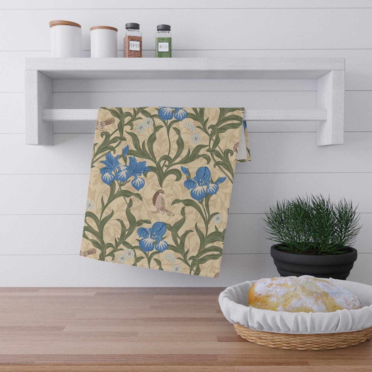 A kitchen tea towel with a William Morris & Co floral pattern featuring blue irises, birds, and a beige background.