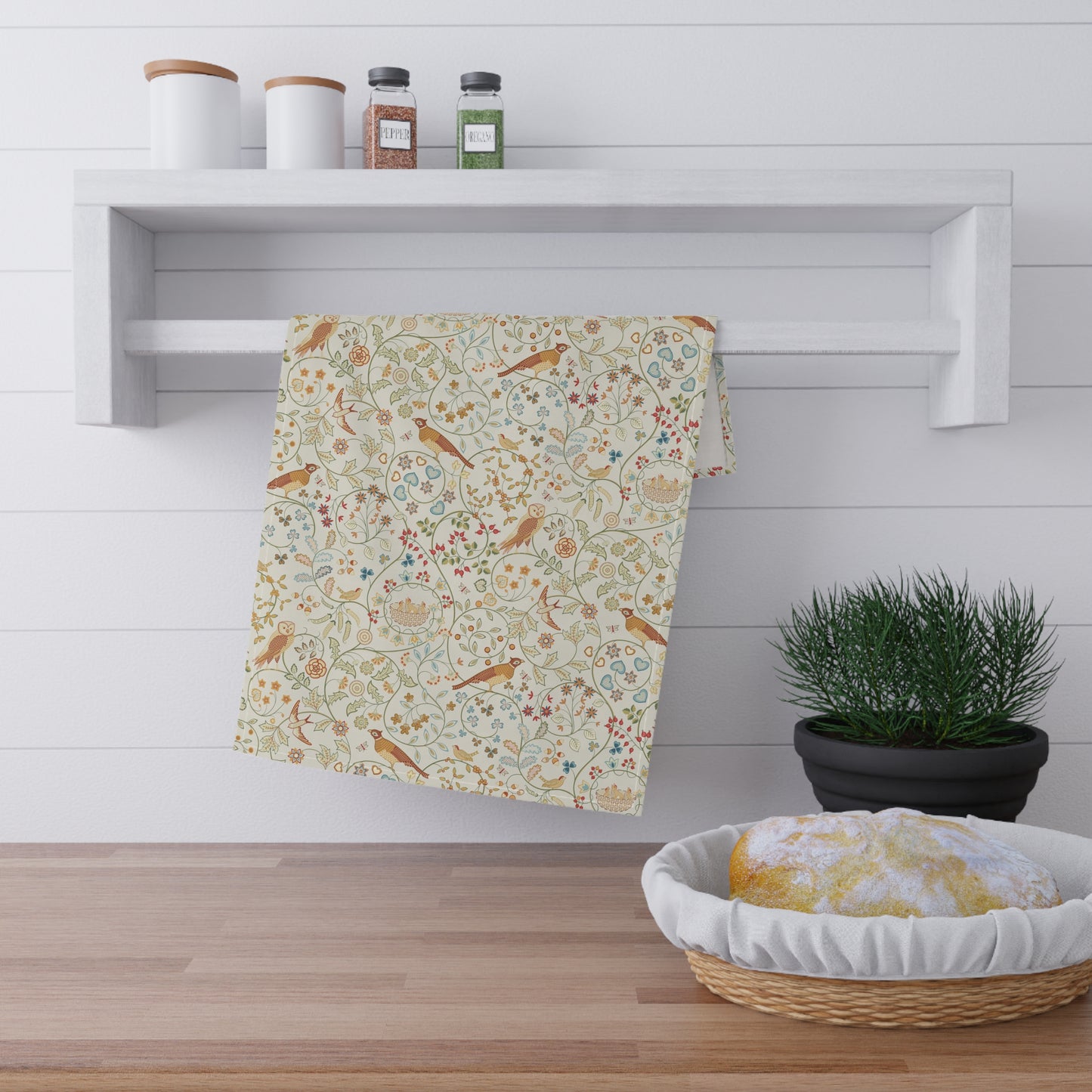Decorative towel with floral and bird pattern hanging on a white wall above a wooden shelf.