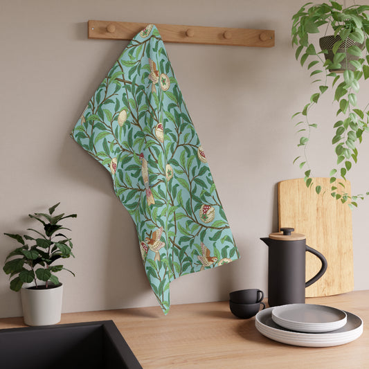 A kitchen tea towel with a blue background featuring bird and pomegranate patterns inspired by William Morris.