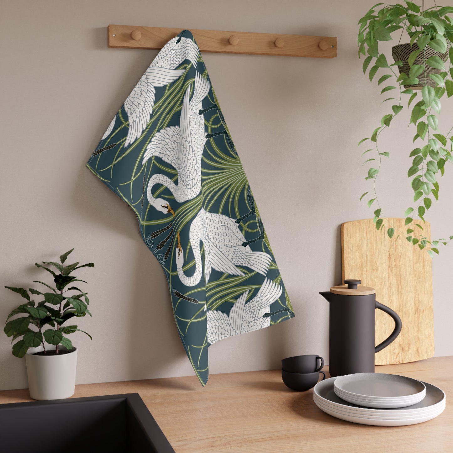 A kitchen tea towel featuring a repeated pattern of a white swan with a green and brownish background, and a set of dishes with cutlery on the side.