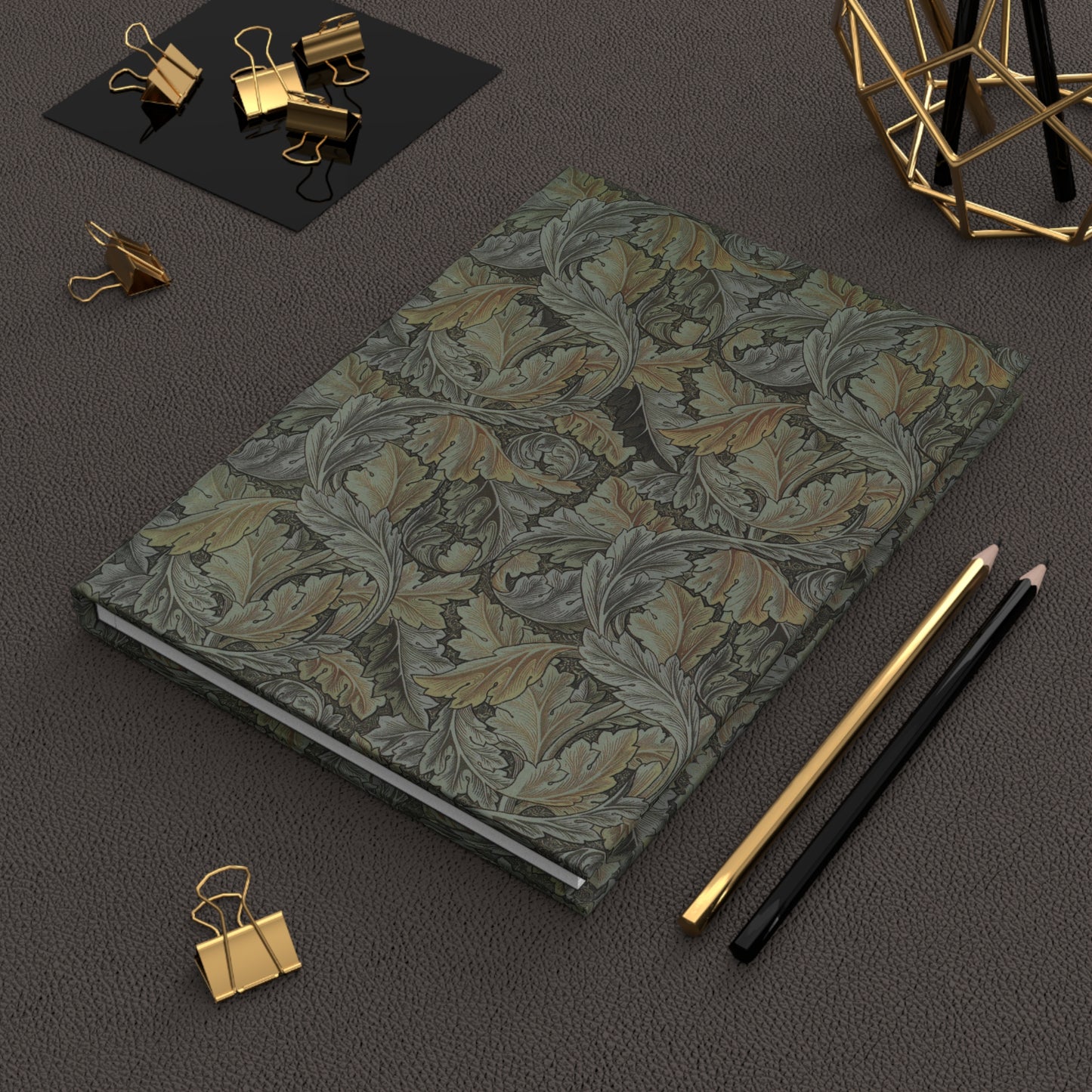 Floral patterned notebook with gold clips and pencils on a dark surface