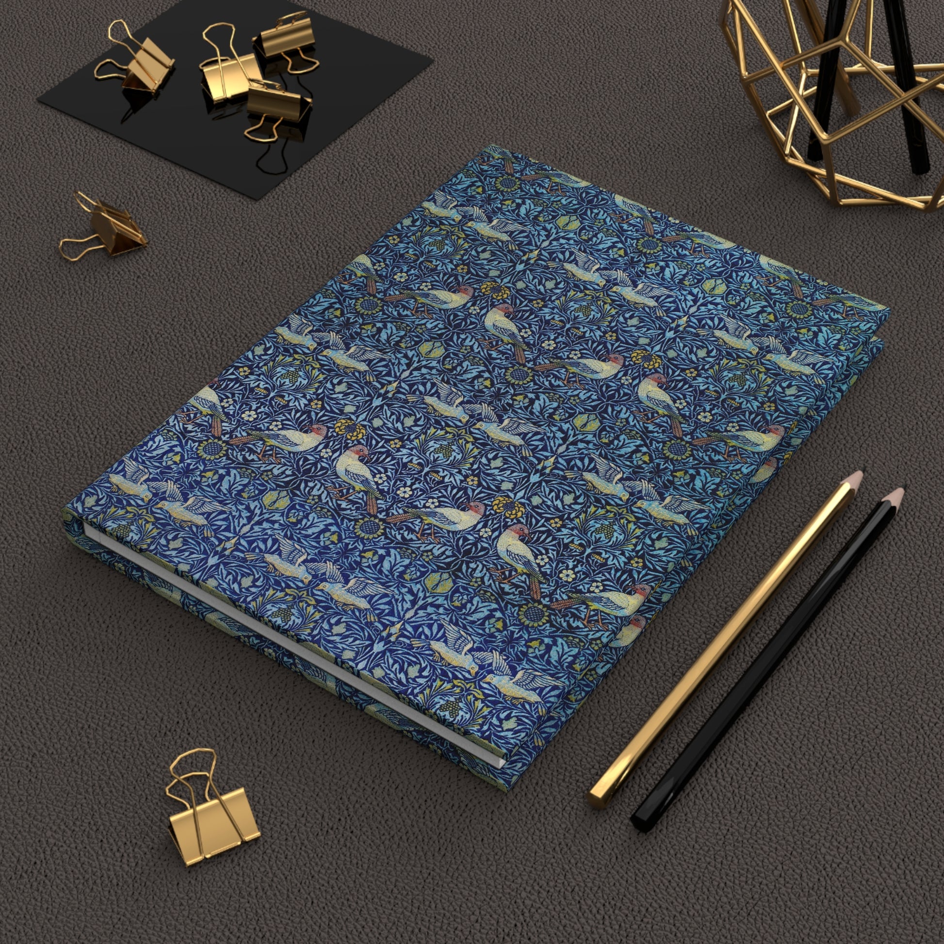 Blue notebook with bird pattern on a dark surface with office supplies