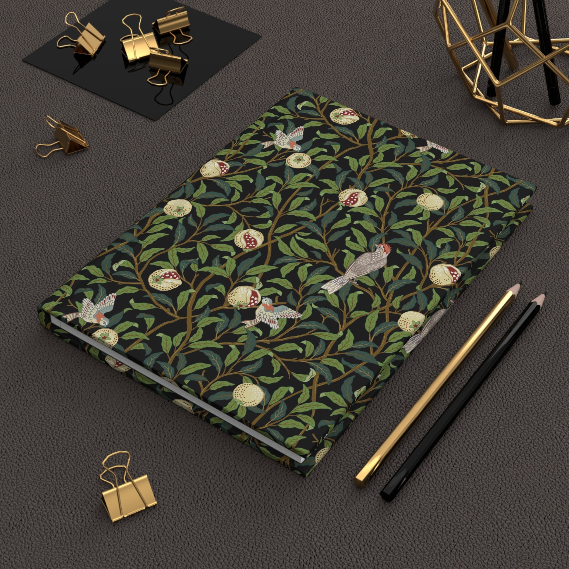 Notebook with a William Morris & Co decorative cover on a dark surface with stationery items.