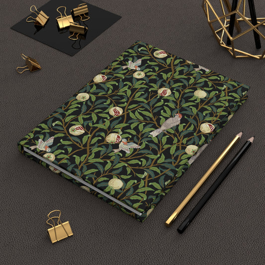 Notebook with a William Morris & Co decorative cover on a dark surface with stationery items.