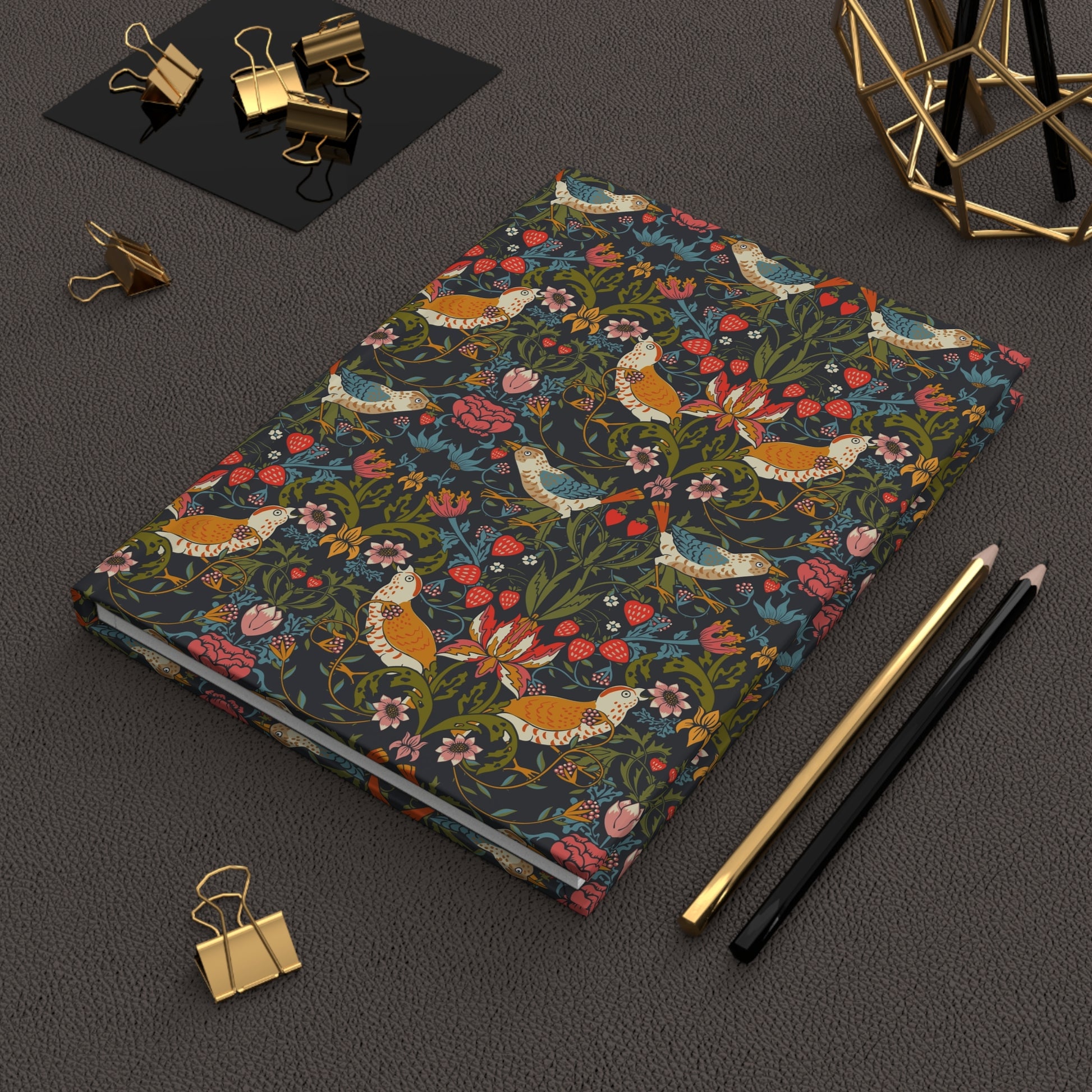 Notebook with floral and bird pattern on a dark surface with office supplies.