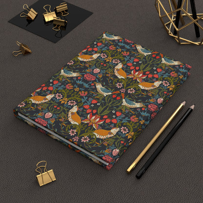Notebook with floral and bird pattern on a dark surface with office supplies.