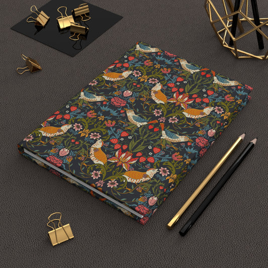 Notebook with floral and bird pattern on a dark surface with office supplies.