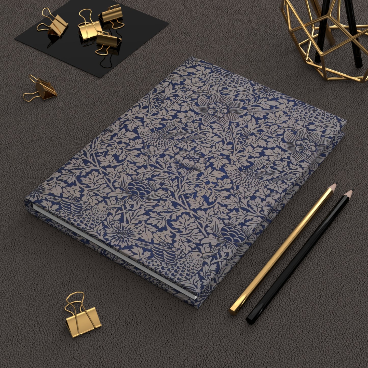Floral-patterned notebook with gold clips and pencils on a dark surface