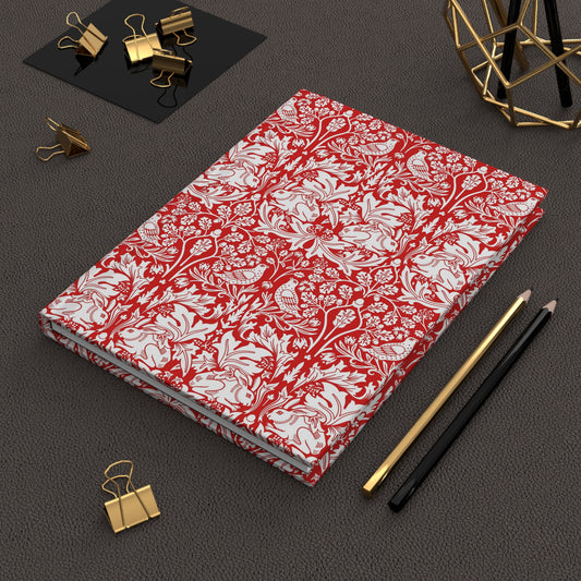 Red and white floral notebook on a dark surface with office supplies.