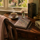 Cozy home scene with a cup of tea, books, and a notebook on a wooden desk by a window.