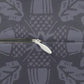Close-up of a zipper with a white pull tab on a dark gray fabric background featuring a repeating light gray abstract pattern.