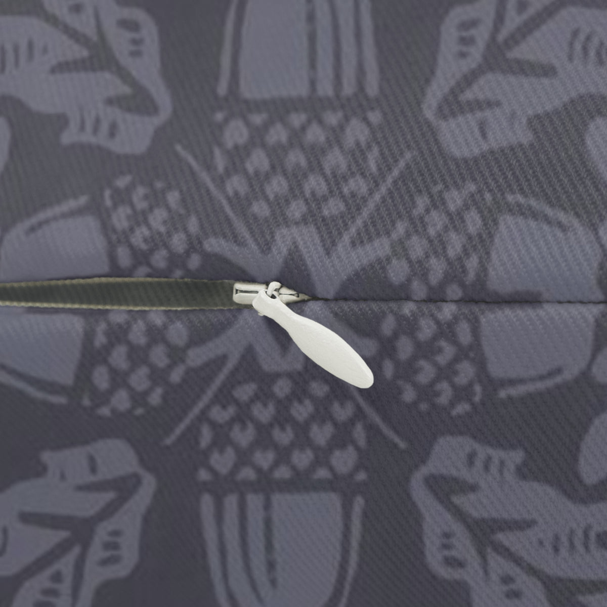 Close-up of a zipper with a white pull tab on a dark gray fabric background featuring a repeating light gray abstract pattern.